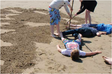 Young people lying on the sand while others rake the sand around them
