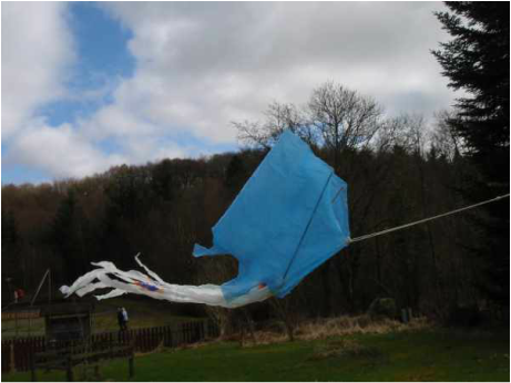 Blue Plastic bag kite flying with trees in the background