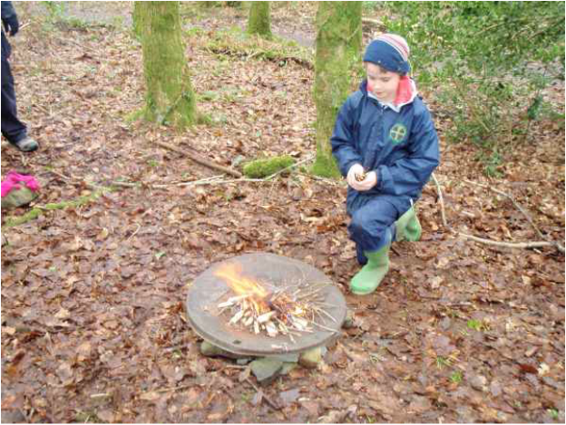 Young boy kneeling in the respect position in front of a fire ready to put some small sticks on it