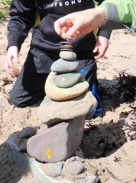 On a beach a child is adding a stone to a tower of balancing stones